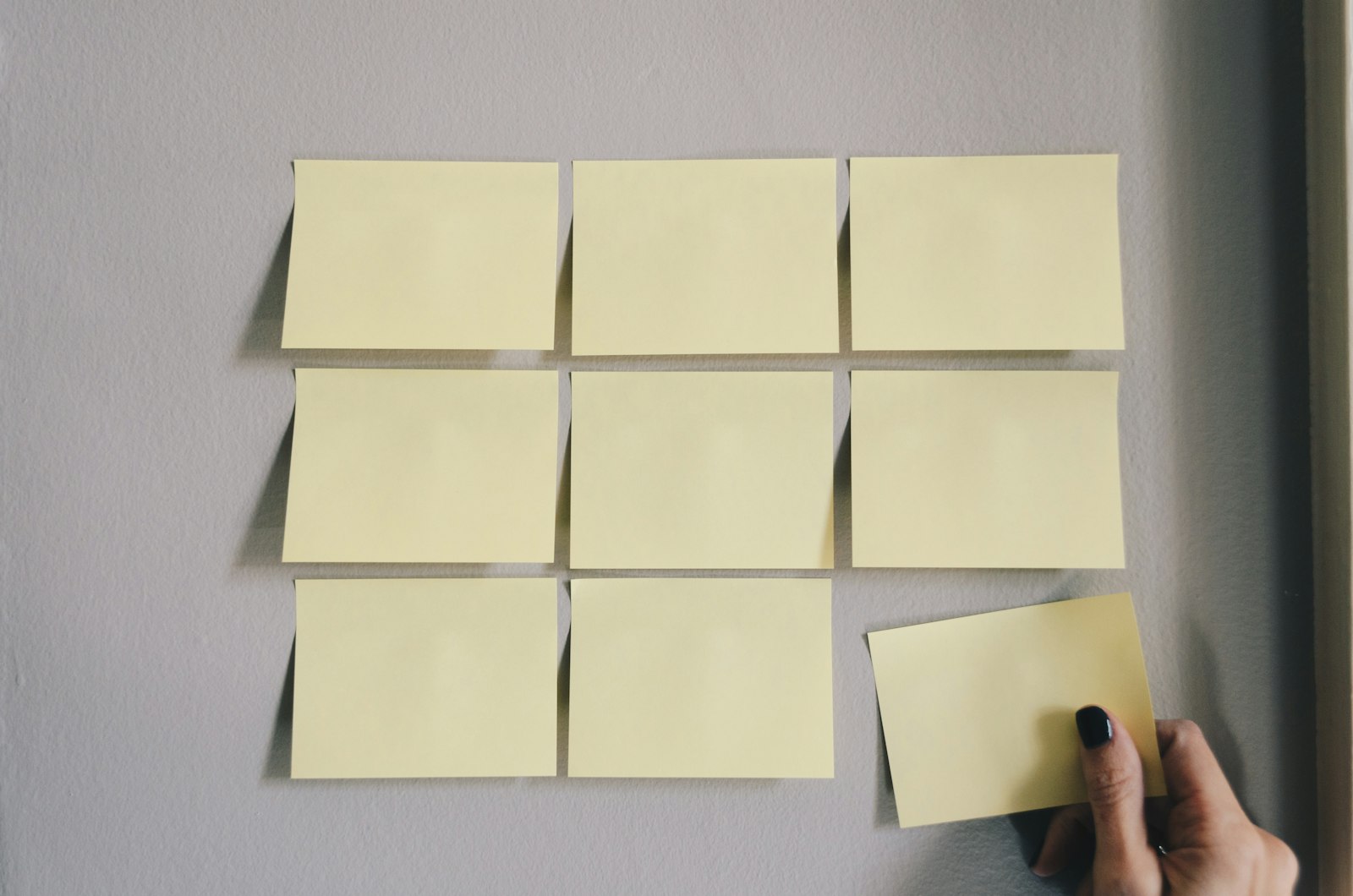A grid of sticky notes on a wall, one being placed by hand